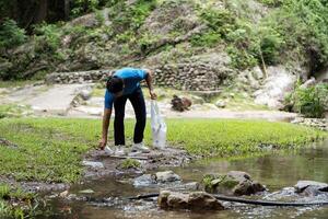 Volunteer Picking Up Waste. A young man collects plastic from a stream during a clean-up event. photo