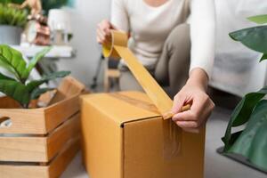 Organizing for a move. Woman sealing a cardboard box with tape in a well-decorated room. photo