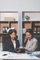 Two women in business attire sitting at a desk with a tablet photo