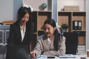 Two asian girls in business attire working on a laptop photo