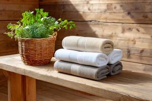 Stacked towels resting on wooden bench with wicker basket and plants in sauna photo