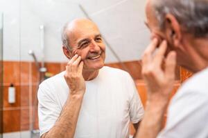 Aged man looking at his reflection in bathroom mirror with happiness, showing the natural aging process with pride. photo
