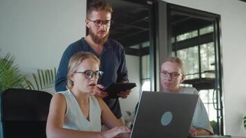 Office workers collaborating on project, utilizing laptop and tablet, while male manager oversees their efforts. Engaging in discussions and strategizing for success. Team management for promotion video