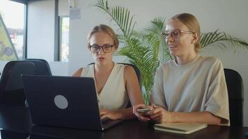 dois conteúdo O Criador estão trabalhando juntos dentro moderno escritório, usando computador portátil e discutindo projeto, mostrando trabalho em equipe e colaboração. conteúdo O Criador crio Novo Ideias juntos para implementação video