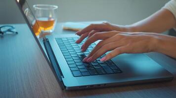 Womans hands adorned with pink nail polish typing on laptop keyboard, working remotely from home while enjoying cup of tea and having glasses nearby for comfort and focus. work of writer video