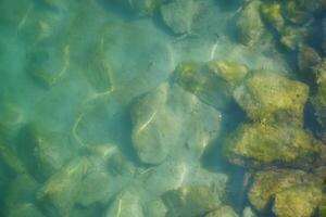 Water surface with stones on the bottom top view. Background abstracted wallpaper texture photo