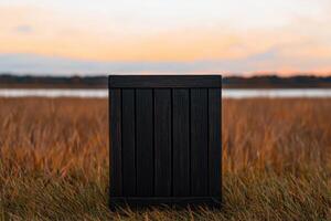 Sunset Landscape A Dark Wooden Box in a Golden Field near a Calm Lake. Peaceful Nature Photography, capturing the serene beauty of photo