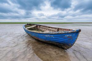 Solitude of an Old Blue Boat on a Sandy Beach A Serene Seascape under a Cloudy Sky. The image captures a weathered boat resting on photo