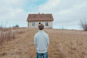 A Solitary Figure Contemplates an Abandoned House in a Desolate Landscape A poignant scene of rural decay, evoking themes of solit photo