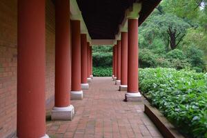 Serene Pathway A Captivating View of Red Columns and Lush Greenery in a Classical Building's Garden. The architectural design crea photo