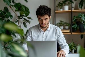 Focused man working on laptop in a modern home office surrounded by plants. A serene and productive workspace, promoting calm and photo