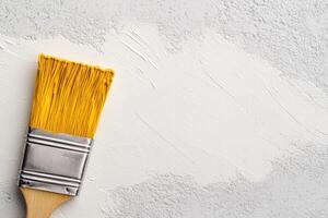 of a paintbrush with yellow bristles against a white textured background. The image is perfect for DIY, home decor, and art projec photo