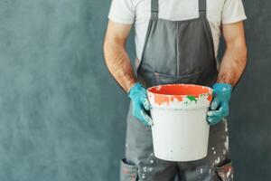 A painter's hands hold a paint bucket, showcasing the tools and effort involved in painting and home improvement projects. The ima photo