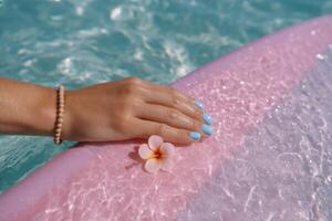 Serene Summer A Woman's Hand with Pastel Nails and a Delicate Flower Resting on a Pink Surfboard by the Pool. A picture of summer photo
