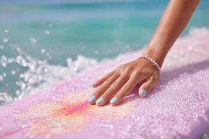 A woman's hand gently rests on a vibrant pink surfboard, the ocean's turquoise waves splashing around. A scene of summer, beach, a photo