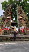 Female tourist walks up stairs into traditional Hindu temple in Ubud, Bali. Ornate stone gate, guardian statues, ceremonial decorations, and sacred atmosphere. video