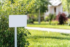 Blank sign near suburban house for advertising or information. Greenery around photo