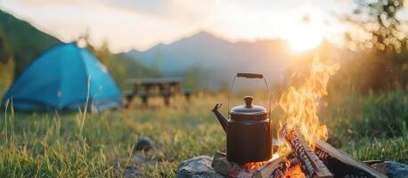 Kettle boils at campsite with bonfire, tent, and sun in mountain backdrop photo