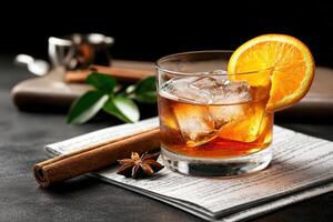 Iced cocktail with orange slice, cinnamon, and star anise on dark background photo