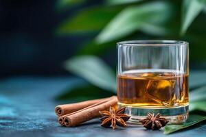 Whiskey with ice, cinnamon, star anise on dark background with tropical leaves photo