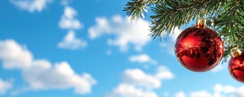 Red ornaments hanging from a pine branch against a cloudy sky photo
