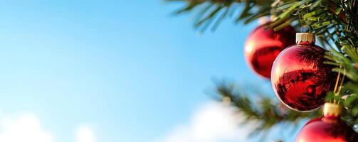 Red ornaments hanging on a Christmas tree against a blue sky photo