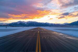 Snowy airport runway at sunset with mountain backdrop photo