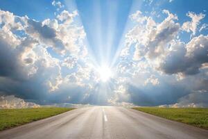 Sunbeams over empty highway road through green fields under dramatic sky photo