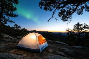 Illuminated tent on mountaintop at sunset under aurora borealis photo