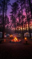 Campfire and tents under colorful sunset sky in forest photo