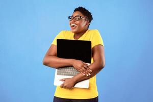 Happy Overweight Black Woman Hugging Laptop Computer With Blank Screen Posing Standing Over Blue Studio Background. Online Technology. Website Advertisement Concept. Mockup photo
