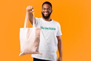 Stop Using Plastic. African Volunteer Man Showing White Eco Bag To Camera Posing Standing On Yellow Studio Background. Consumerism And Ecology, Plastic-Free Lifestyle photo