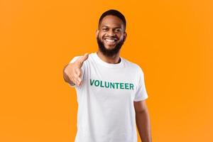 Cheerful Volunteer Guy Stretching Hand For Handshake Greeting To Camera Standing Posing In Studio Over Yellow Background. Voluntary Work, Join Our Volunteering Team Concept photo