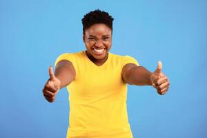I Like It. Happy Plus-Size Black Woman Gesturing Thumbs Up With Both Hands Approving Something Posing Over Blue Studio Background, Smiling To Camera. Thumbs-Up Gesture Concept photo