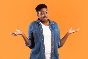 I Don't Know. Puzzled Plus-Size Black Woman Shrugging Shoulders Standing Posing Over Yellow Studio Background, Looking At Camera. Shoulder Shrug Gesture Concept. photo