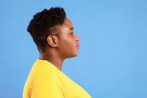 Profile Portrait Of Overweight African American Woman With Short Haircut Posing Looking Aside Over Blue Studio Background. Side-View Shot Of Plus Size Black Female. Empty Space For Text photo