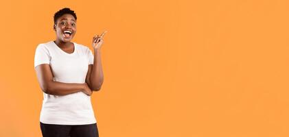 Happy Plus-Size Black Lady Pointing Finger Up Having Great Idea Standing Near Copy Space Advertising Your Text Posing On Yellow Studio Background, Smiling To Camera. Eureka, Inspiration Moment photo