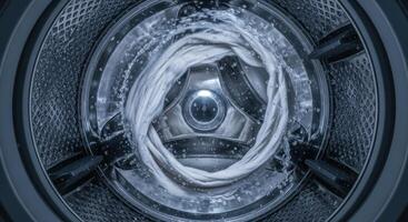 Inside a washing machine drum, white clothes spin with water during a cleaning cycle. photo