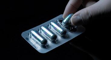 Close up of a gloved hand taking an iridescent capsule from a blister pack photo
