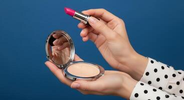 Woman hands holding an open compact powder case and a pink lipstick on blue background. photo