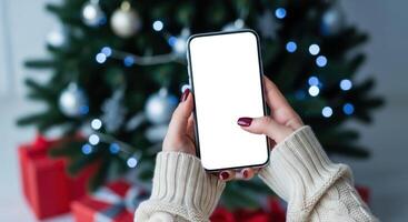 Woman holding a smartphone with blank white screen in front of a christmas tree. photo