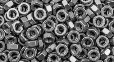Close up top down view of a dense pile of numerous small hexagonal matte silver metal nuts photo