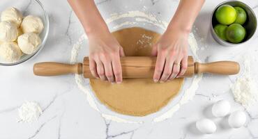 Woman hands rolling dough with a wooden pin on a marble counter, top view photo