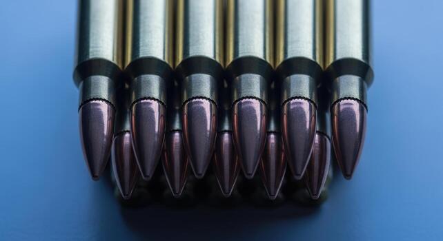 Close up view of shiny rifle ammunition cartridges neatly arranged on a blue surface photo
