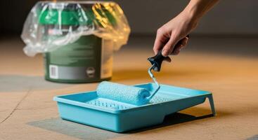 Hand holding a paint roller with blue paint in a tray for home renovation work photo