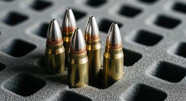 Close up of five shiny brass and silver bullets in a grey foam ammunition tray. photo