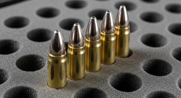 Close up of five brass and silver bullets standing upright in a grey foam ammunition tray photo
