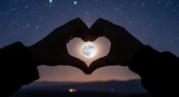 Hands forming a heart shape around the full moon in a beautiful starry night sky photo