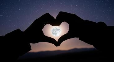 Silhouette of hands forming a heart shape around a full moon in a starry night sky photo