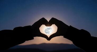 Silhouetted hands forming a heart shape around the full moon in a starry night sky photo
